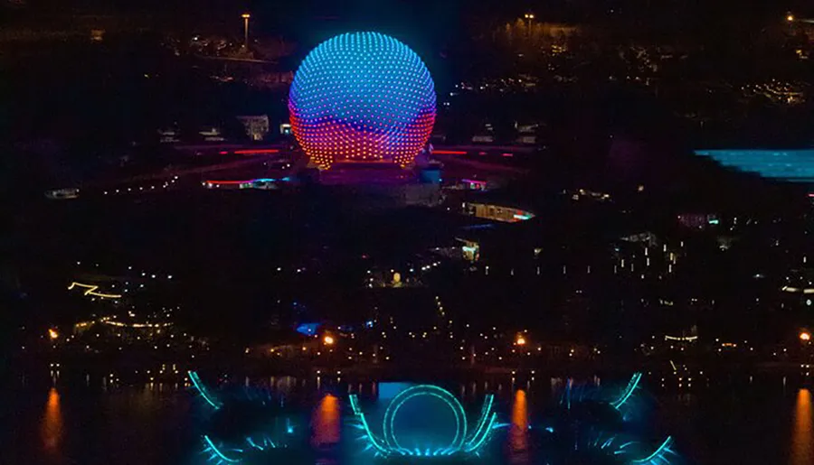 The image shows a striking night view of a brightly lit spherical structure reflecting over water, creating a mesmerizing mirror image.