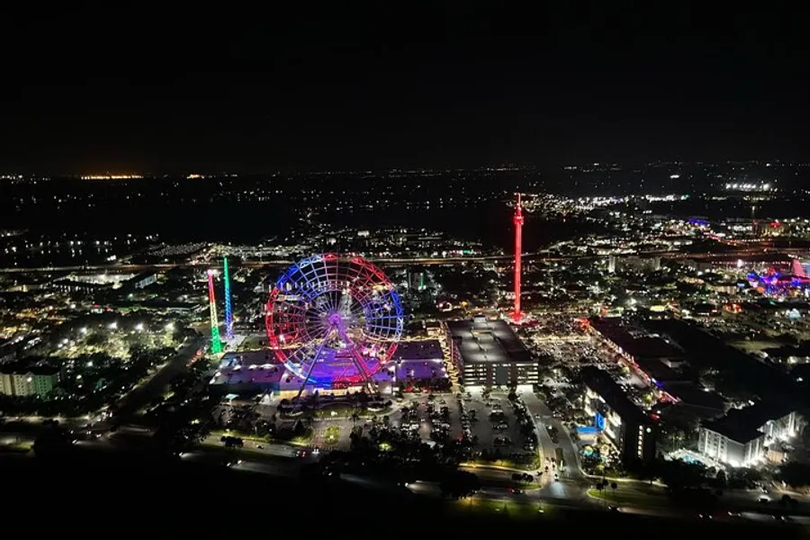 The image shows a vibrant night view of a cityscape featuring a brightly lit Ferris wheel and colorful illumination from nearby attractions and buildings.
