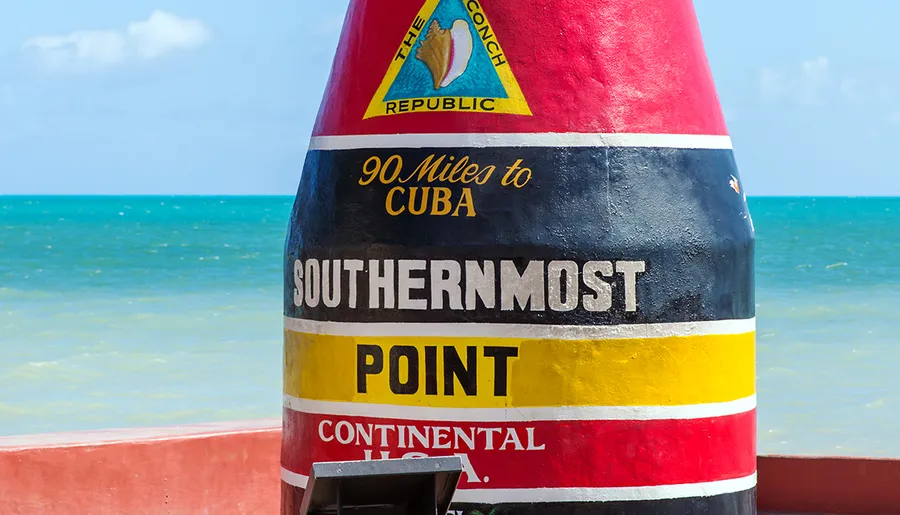 The image shows the iconic, buoy-shaped Southernmost Point marker in Key West, Florida, indicating that Cuba is 90 miles away.