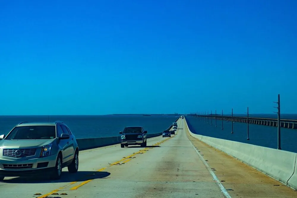 Vehicles travel on a long bridge over a serene blue sea under a clear sky