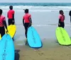 A group of five individuals wearing wetsuits with student printed on the back stand by colorful surfboards on a sandy beach likely preparing for a surf lesson