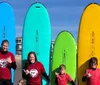 A group of five individuals wearing wetsuits with student printed on the back stand by colorful surfboards on a sandy beach likely preparing for a surf lesson