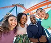 A group of four people smiling together in front of a roller coaster with a small inset image of dolphins swimming underwater