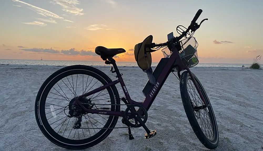 A bicycle is parked on a sandy beach with a scenic sunset in the background