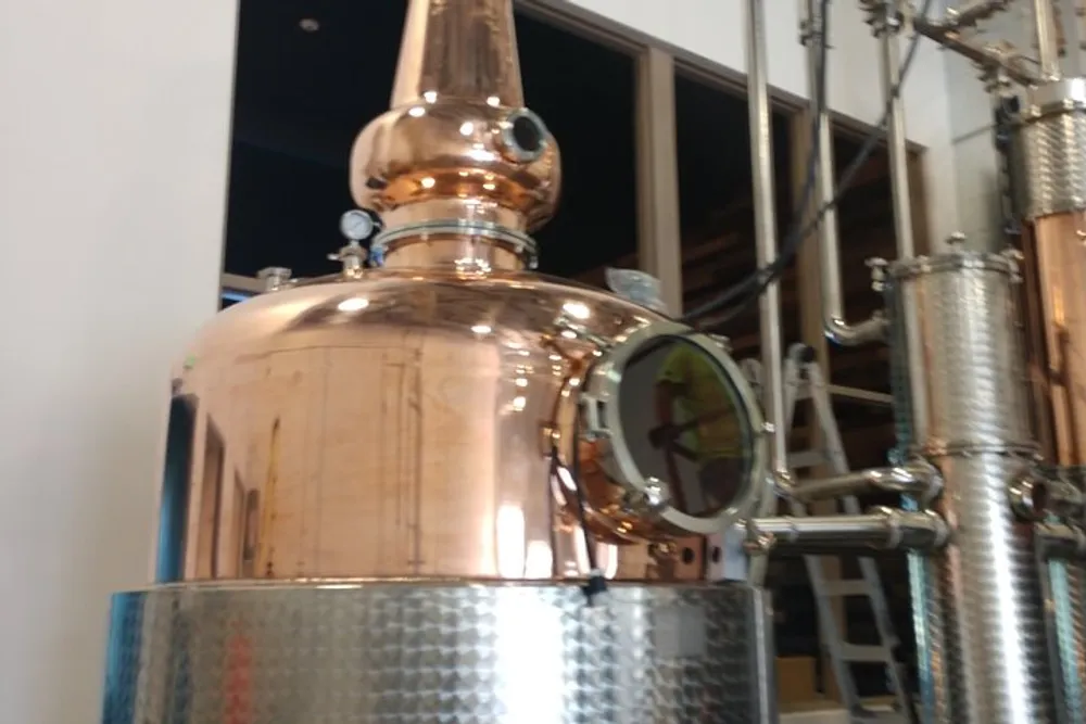 The image shows a shiny copper distillation apparatus possibly used in a brewery distillery or chemical process facility