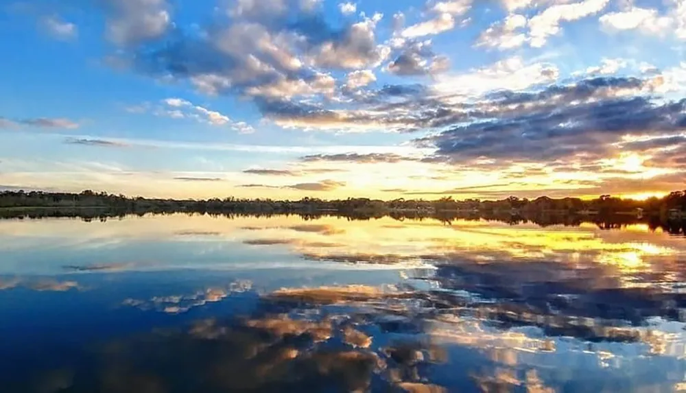 The image shows a dramatic sunset with a sky full of clouds reflected on the calm surface of a large body of water suggesting a tranquil evening scene