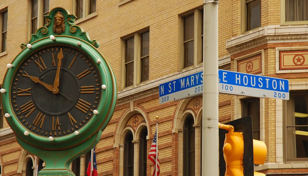The image features an ornate street clock in the foreground with intersecting street signs for N St Marys and E Houston set against a backdrop of urban architecture and flags including the United States and Texas flags