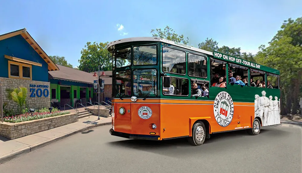 A trolley bus full of passengers is driving past the San Antonio Zoo entrance