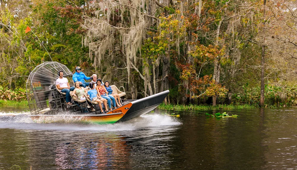 A group of individuals is enjoying a ride on an airboat through a waterway lined with trees and Spanish moss