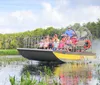 An airboat with passengers is gliding through a sunny and lush wetland