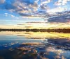 Two people are kayaking on tranquil waters under a pastel sunset sky