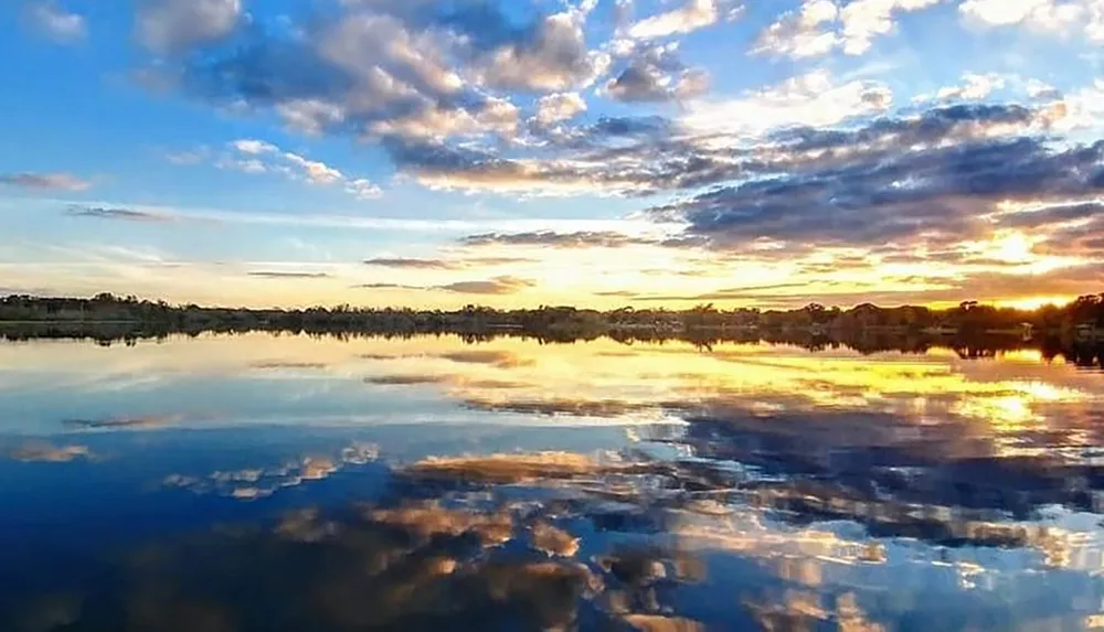 The image shows a serene landscape with a vivid sunset reflecting off the smooth surface of the water creating a beautiful mirror image of the sky and clouds