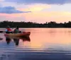 Two people are kayaking on tranquil waters under a pastel sunset sky