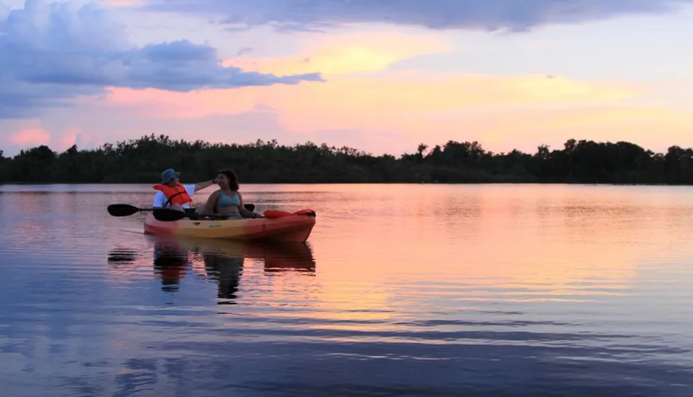 Two people are kayaking on tranquil waters under a pastel sunset sky