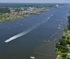 The image shows an aerial view of a wide river with a variety of boats and a cityscape in the background creating a lively scene of waterway transportation and urban life