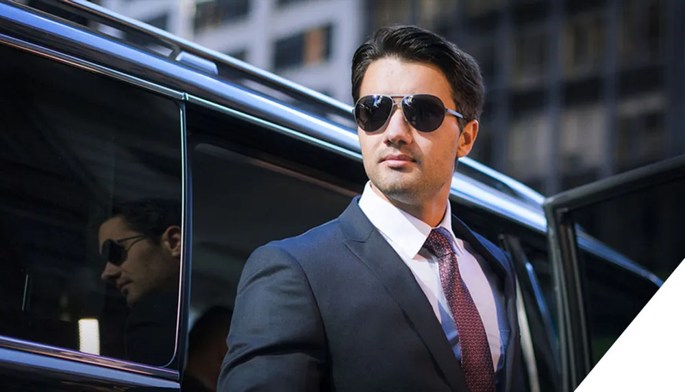 A person in a suit and sunglasses is getting out of a luxury car