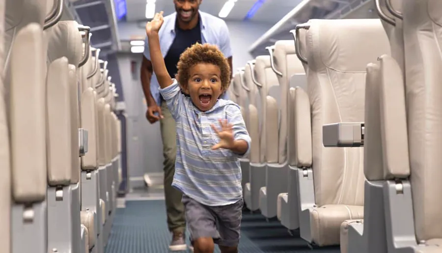 A joyful child is running down the aisle of an airplane with a smiling man in the background.
