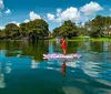 Three individuals are enjoying paddleboarding on a calm waterway with lush greenery in the background and a dock to one side