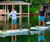 Three individuals are enjoying paddleboarding on a calm waterway with lush greenery in the background and a dock to one side