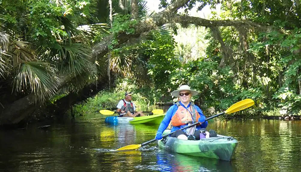 Two people are kayaking along a peaceful tree-lined waterway enjoying the outdoors