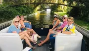 A group of friends is enjoying a leisurely boat ride along a canal lined with lush greenery.