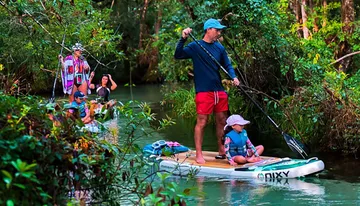 A group of people is enjoying paddleboarding and kayaking along a serene, forest-lined waterway.