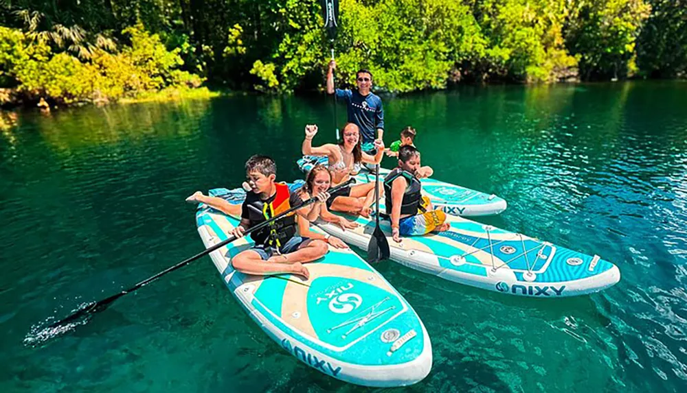 A group of people are joyfully paddleboarding on a clear tranquil body of water surrounded by lush greenery