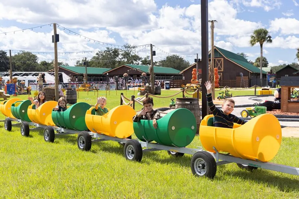 Children are enjoying a ride in a caterpillar-shaped train at an outdoor event under a sunny sky