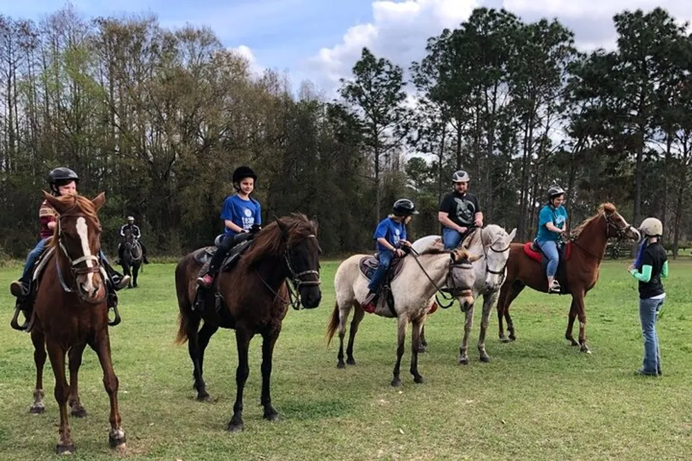 A group of riders on horseback are gathered in a field possibly taking part in an equestrian lesson or on a leisurely ride