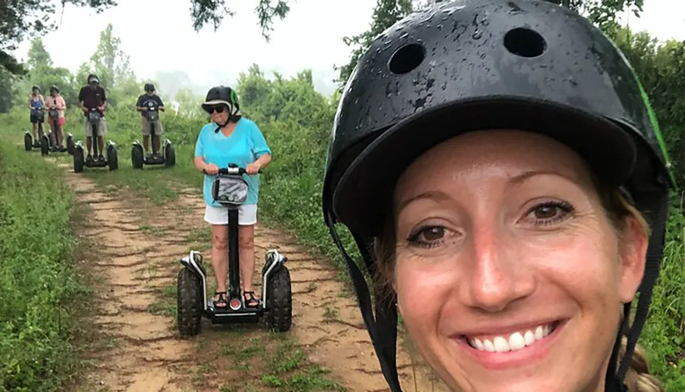 A group of people are enjoying a Segway tour on a forest trail with a smiling woman in the foreground taking a selfie