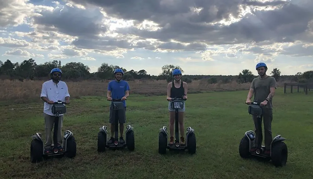 Four people wearing helmets are standing on Segways in an open field under a cloudy sky