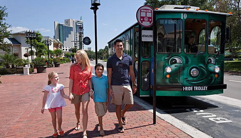 A family walks hand in hand on a sunny day next to a green trolley showing a sign that reads Out of Service