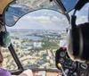 A person wearing headphones is piloting a helicopter providing an aerial view of a landscape with water bodies and urban developments