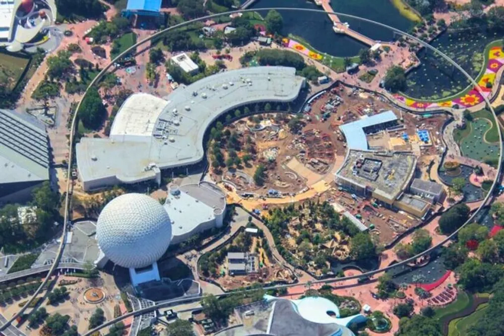 An aerial view of a theme park showing various attractions and ongoing construction with a distinctive geodesic sphere as its centerpiece