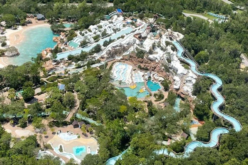 The image shows an aerial view of a water park with various swimming pools water slides and a lazy river surrounded by lush greenery