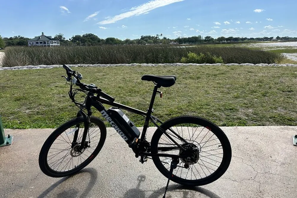 A bicycle is parked on a paved surface with a scenic view of grassy terrain and a white building in the distance under a partly cloudy sky