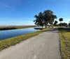 A serene pathway runs alongside a waterway flanked by green grass and trees under a clear blue sky