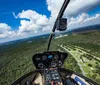 The image shows the cockpit view from a helicopter overlooking a lush landscape with roads and trees taken from a high vantage point mid-flight