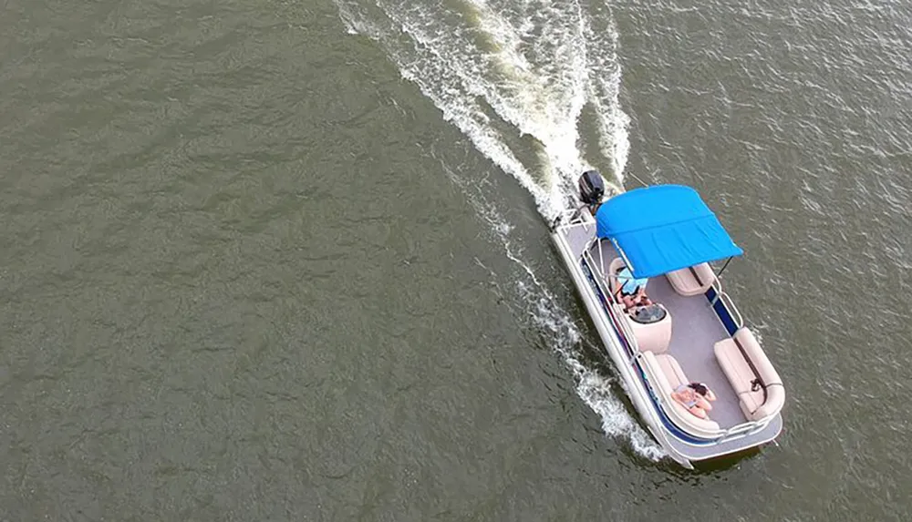 A pontoon boat with a blue canopy is cruising on the water creating a wake behind it