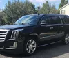 A black Cadillac Escalade SUV is parked on a suburban street in front of a house under a clear sky