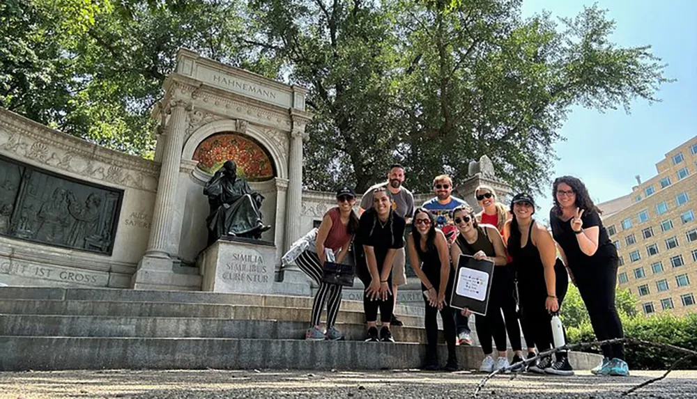 A group of people poses for a photo on the steps of a monument with a seated statue and inscriptions