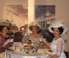 Three women dressed in vintage clothing with elaborate hats are having a cheerful conversation in an elegantly furnished room