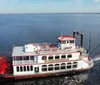 This image features a large red and white paddlewheel riverboat docked beside a calm body of water under a clear blue sky