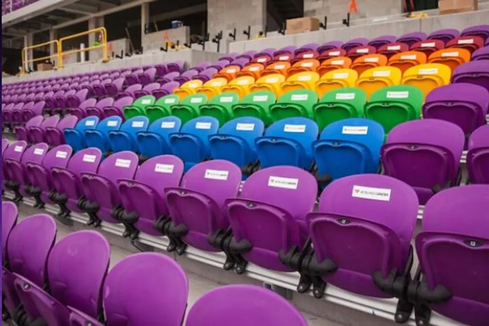 The image shows a colorful array of empty stadium seats in hues of purple green yellow and orange with some seats labeled as RESERVED