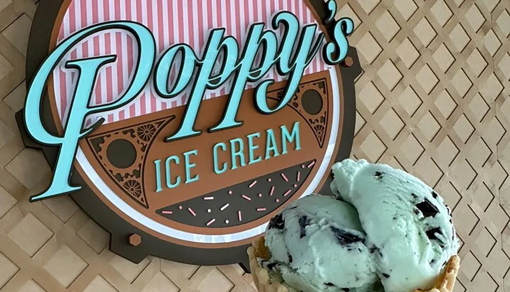 A scoop of mint chocolate chip ice cream in a cone is showcased against the background of a Poppys Ice Cream shop sign