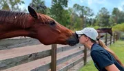 A person is affectionately kissing a horse on the nose over a wooden fence.