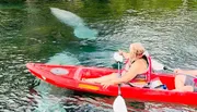 Two people are kayaking on clear water with a manatee visible underneath.