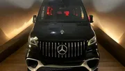 A black Mercedes-Benz van is parked indoors, illuminated by soft lighting that highlights its luxury front grille design.