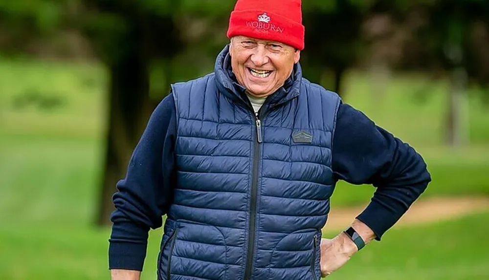 A person is wearing a red hat and blue vest smiling widely in an outdoor setting