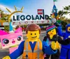 This image features costumed characters resembling LEGO figures in front of the LEGOLAND Florida entrance with colorful LEGO sculptures and the parks sign in the background